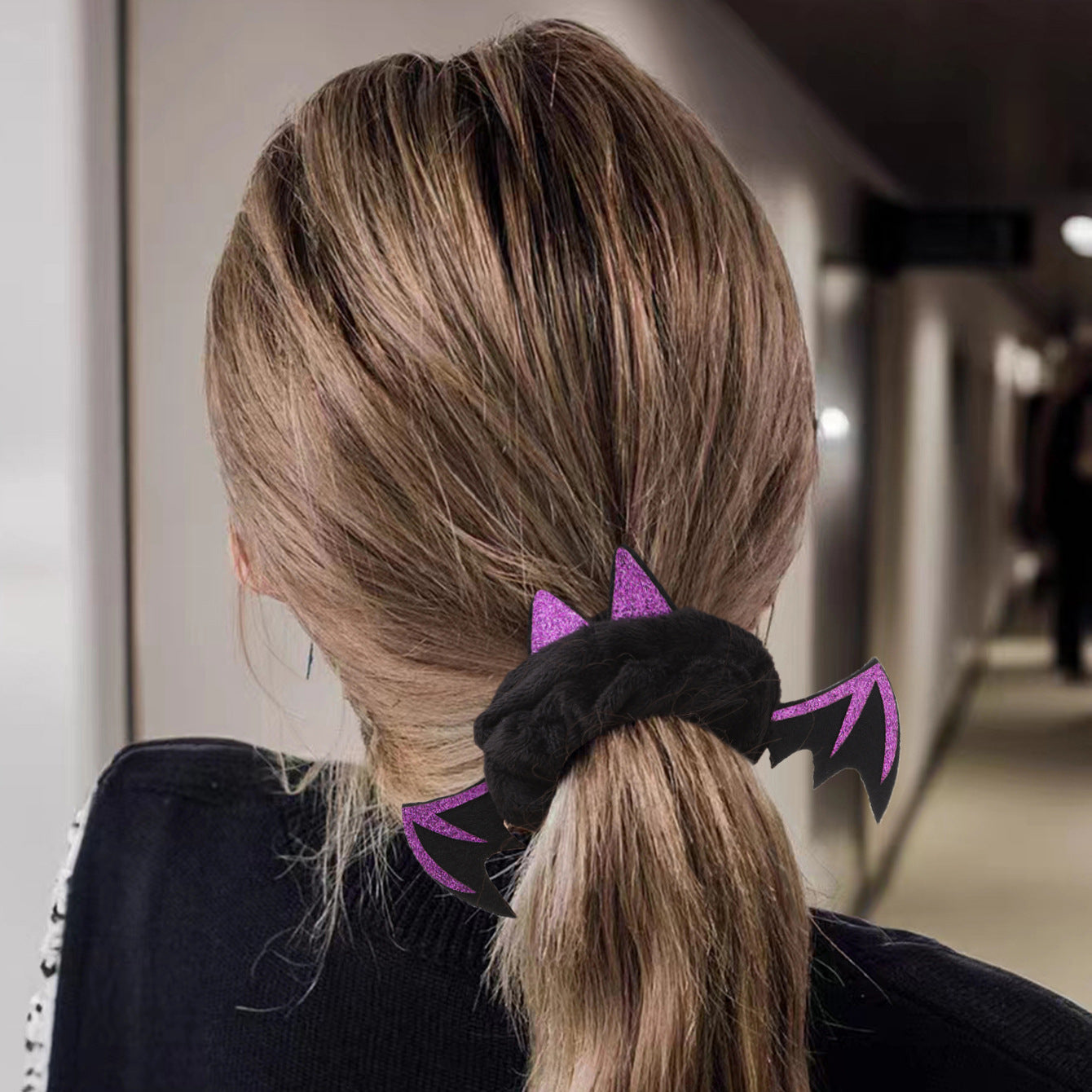 A black and purple bat wing scrunchie styling a ponytail for Halloween.