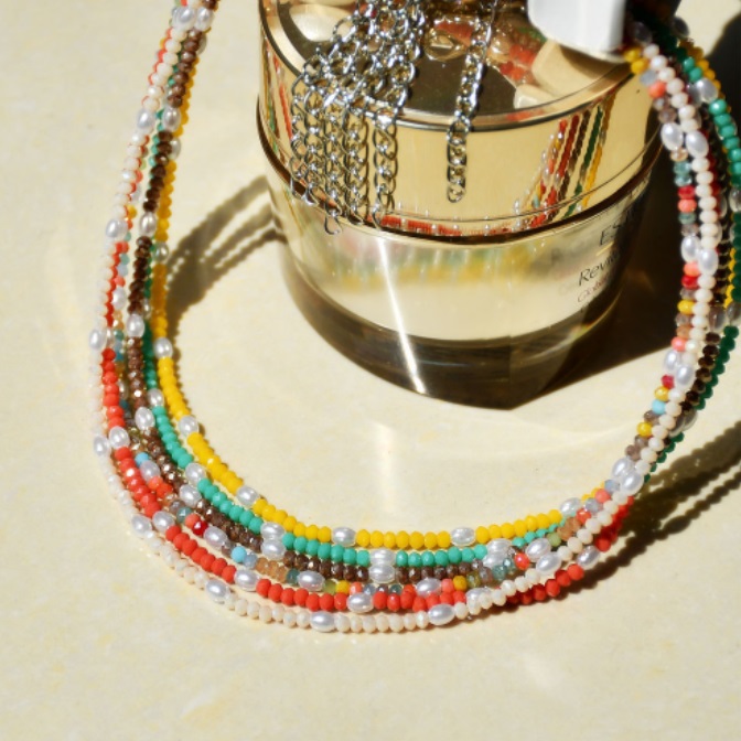 A vibrant multi-coloured beaded necklace displayed elegantly with a perfume bottle, highlighting its summer style.