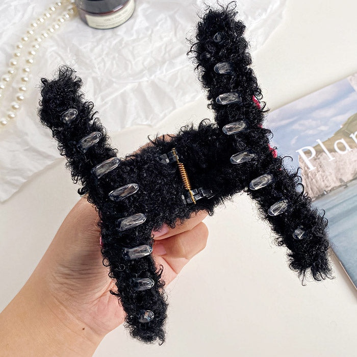 A black fuzzy hair claw clip with clear plastic grips, shown in detail.
