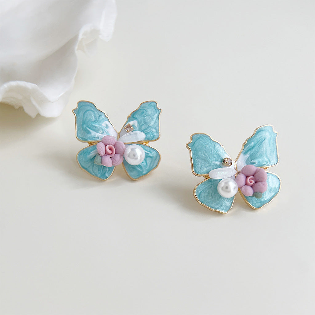 Styled shot of the blue butterfly earrings next to pink flowers, highlighting the pearl accents.
