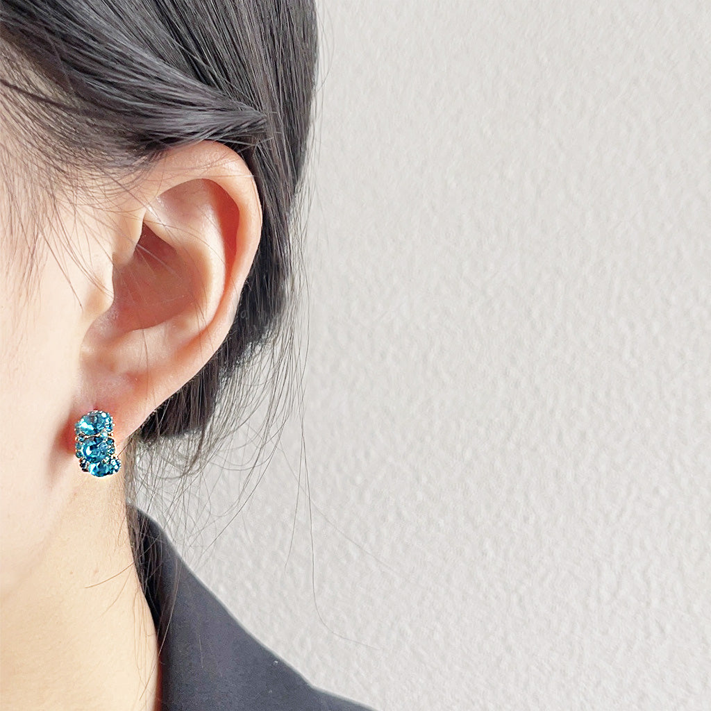 A woman models the sparkling blue rhinestone and gold stud earrings, showing how they catch the light.