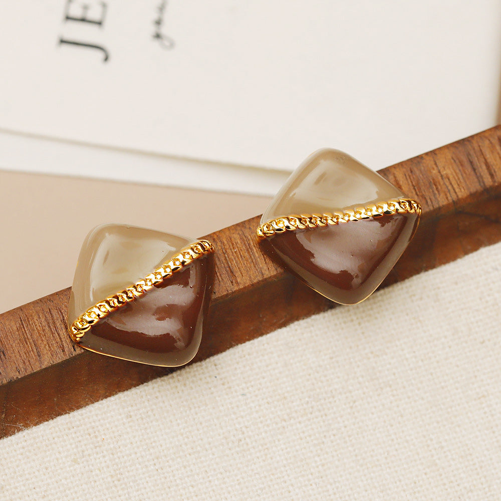 A pair of brown stone-like enamel earrings with gold accents displayed on a wooden surface.