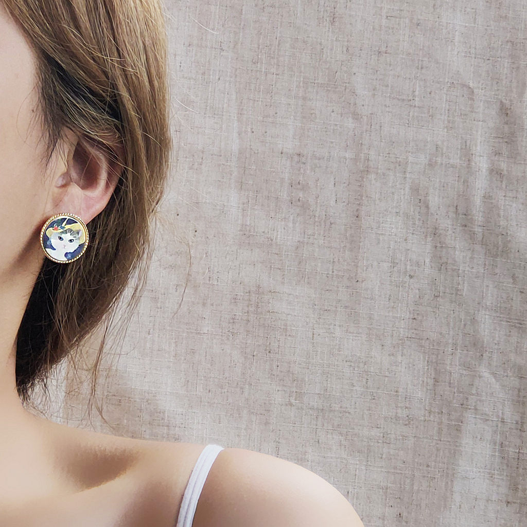 A model showcasing the Round 14k Gold Frame Cat Painting Stud Earring