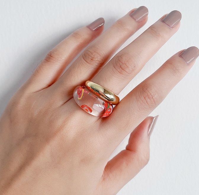 A close-up of the fruit acrylic ring being worn, showing its vibrant colors and clear resin material.