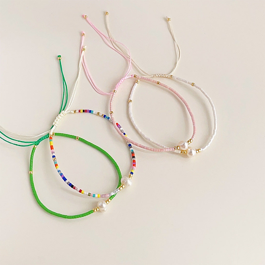 A collection of four colorful handwoven bracelets with pearl and gold accents.