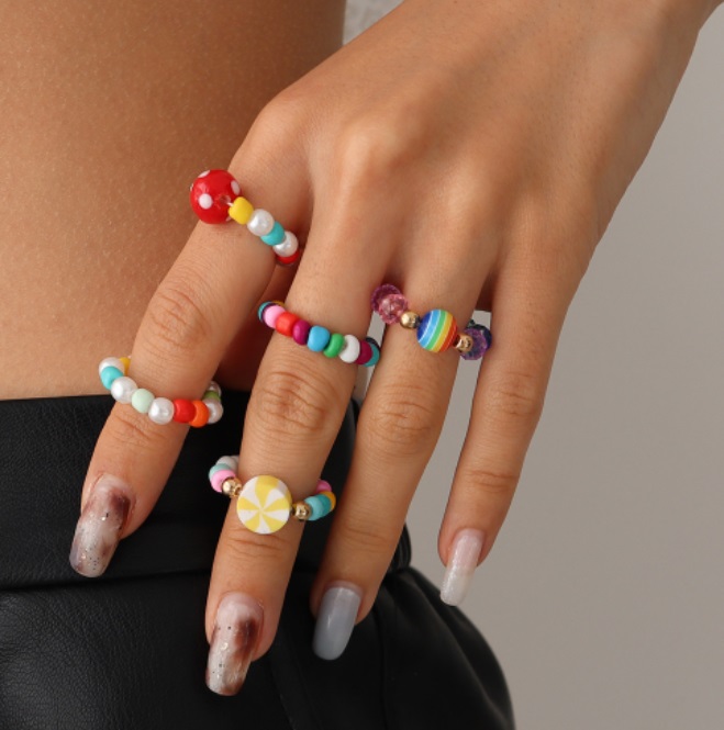 A close-up of a hand wearing multiple styles of colorful beaded rings.