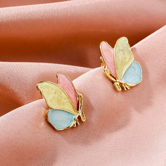 Colorful butterfly earrings displayed on a pink fabric background