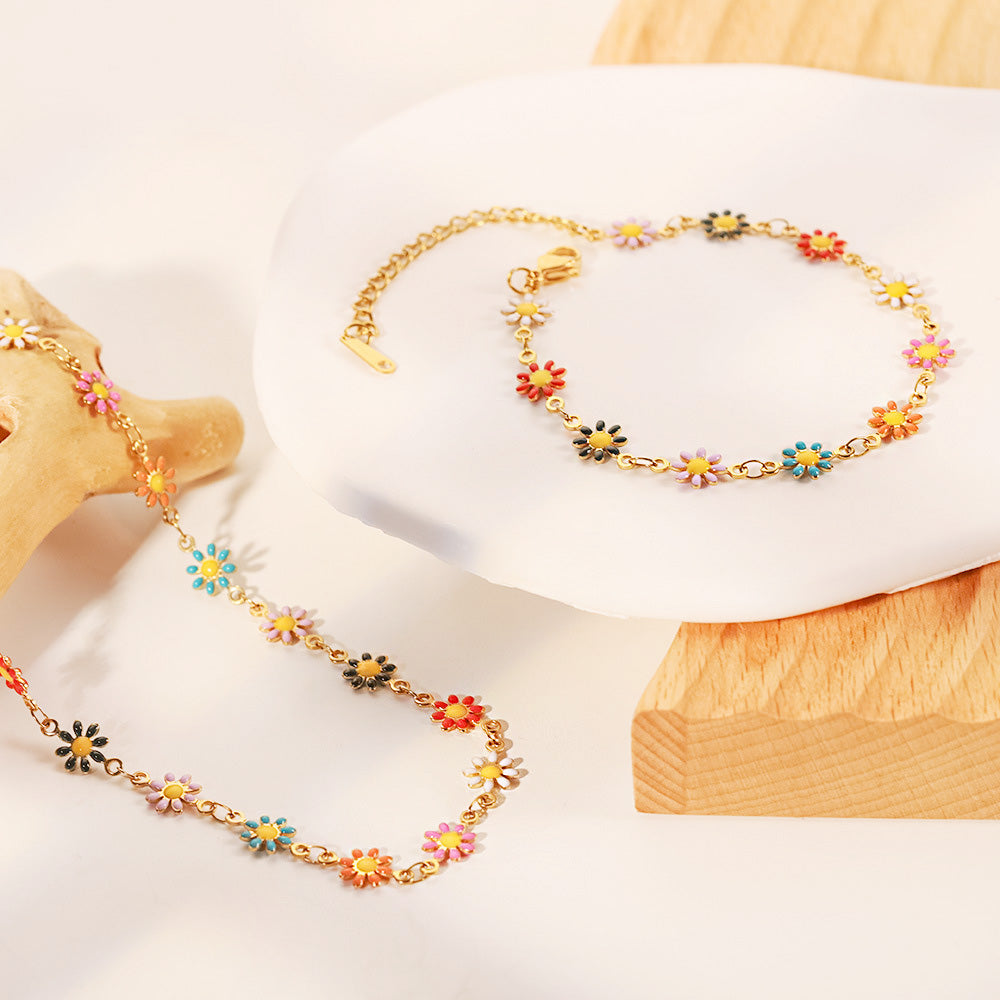 A pair of gold chain bracelets with colorful and white enamel daisy charms