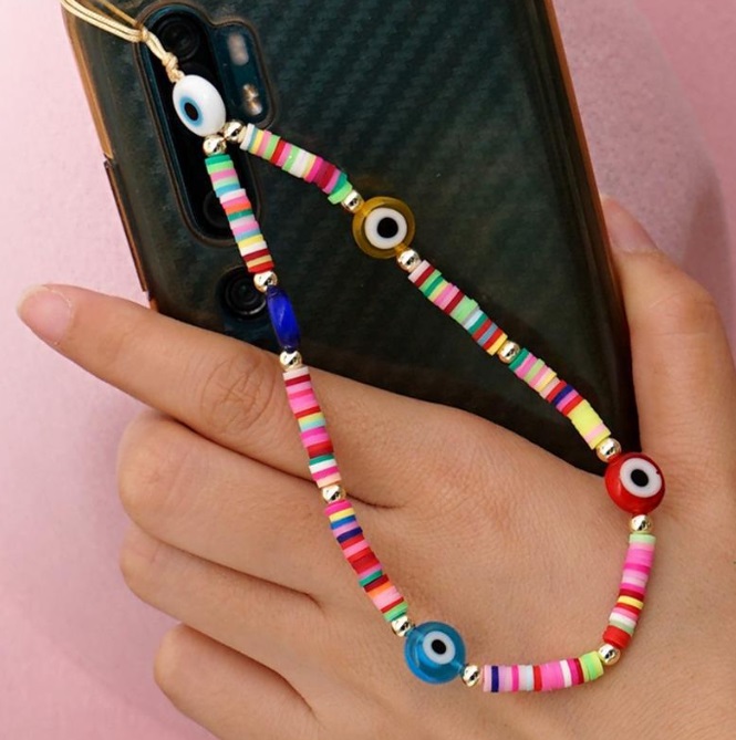A colorful beaded phone charm with eye-shaped beads attached to a black smartphone.