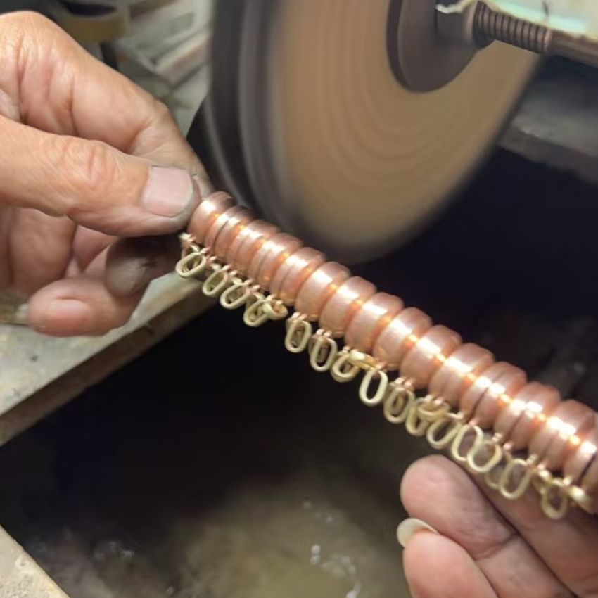A close-up of the grinding process on a custom copper bracelet at the JR Fashion Accessories workshop.