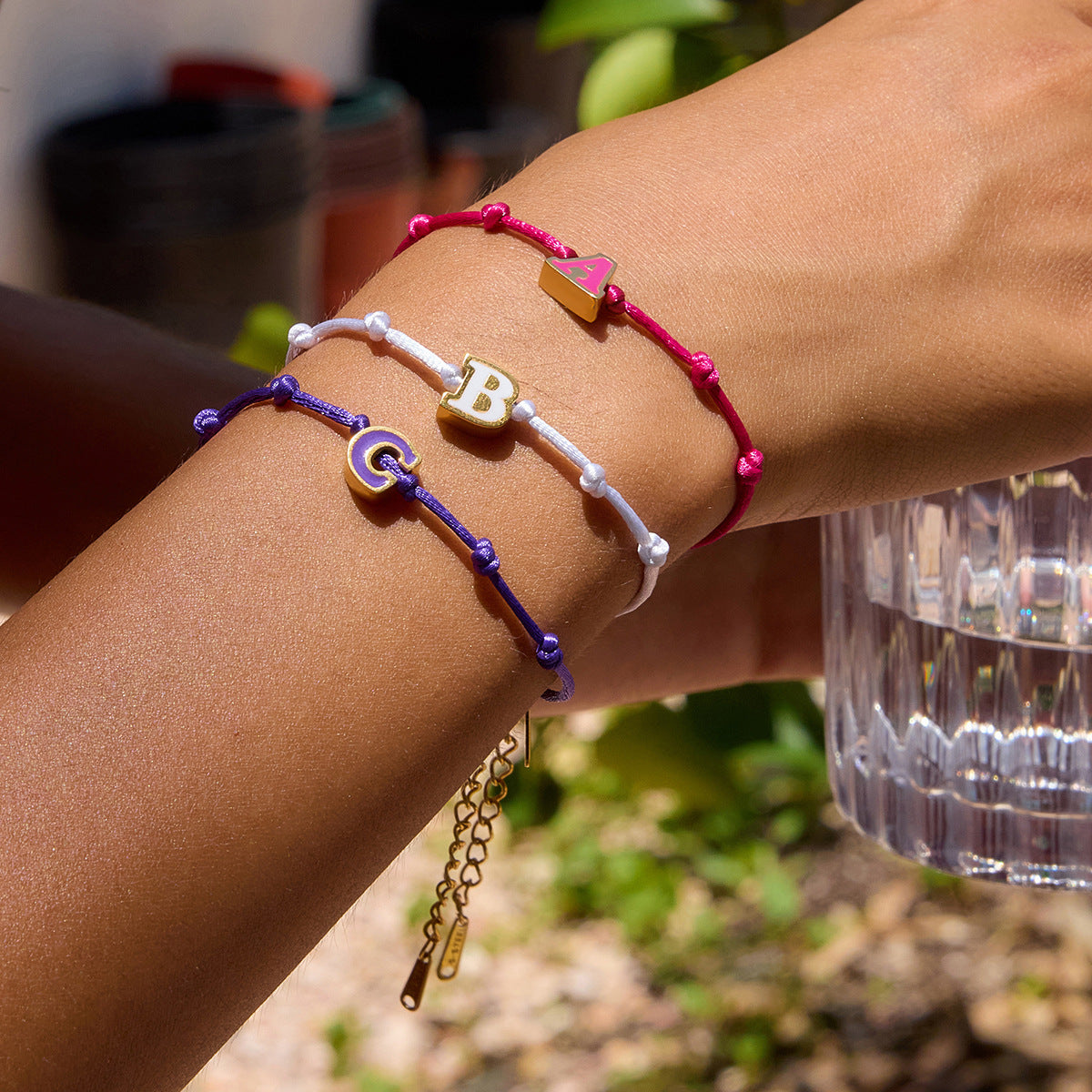 Model wearing a stack of three adjustable friendship bracelets with custom A, B, and C enamel letter charms