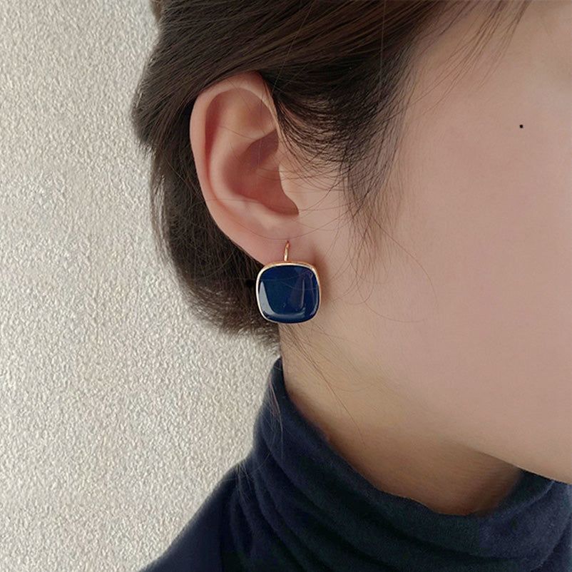 A woman modeling the chic navy blue enamel square hoop earrings