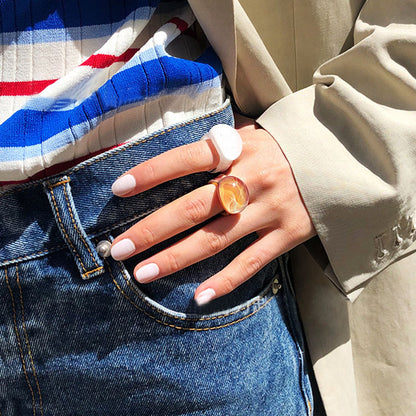 A person wearing the transparent orange glass ring, paired with a stylish outfit.
