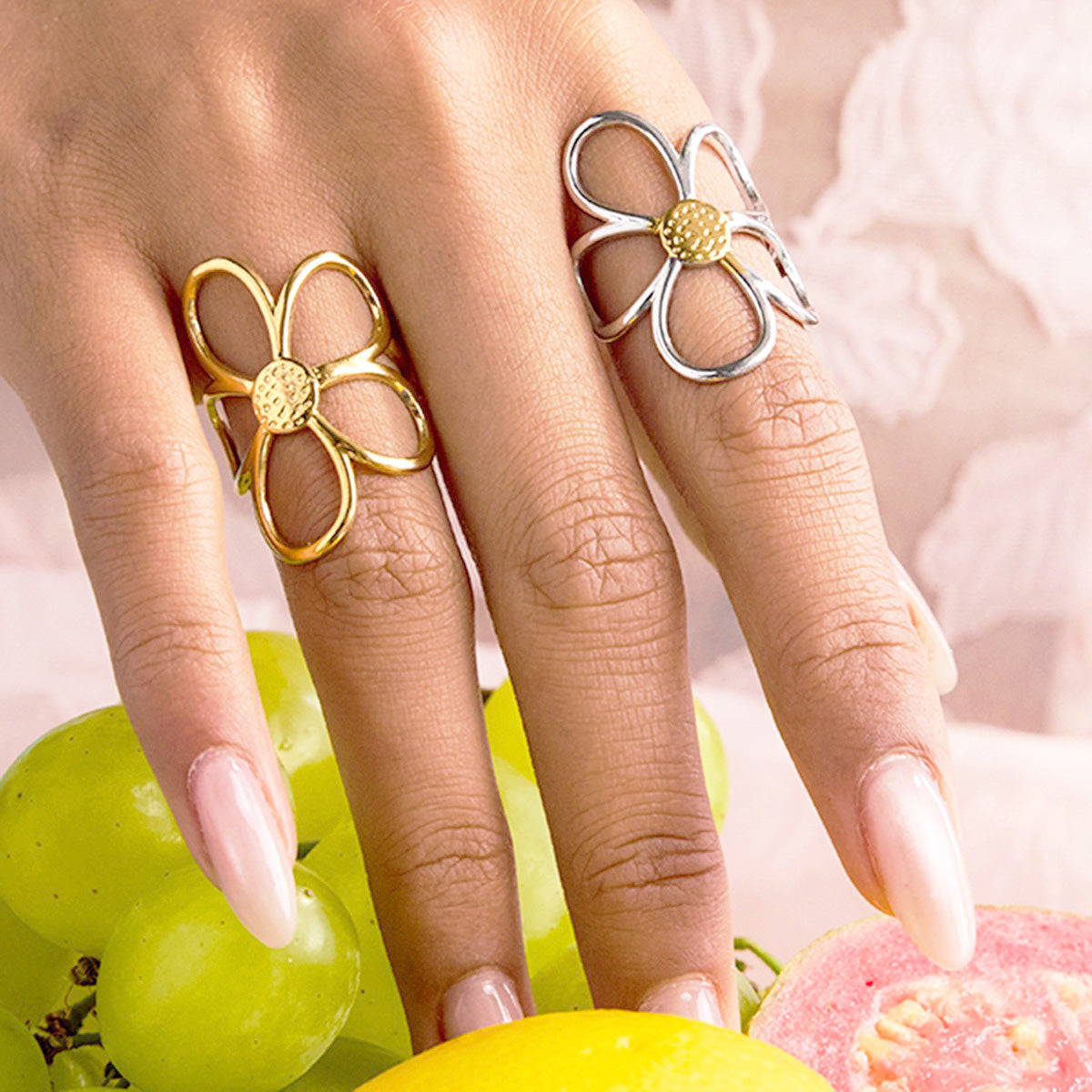 A model's hand adorned with gold and silver daisy rings, showcasing their stacking potential.