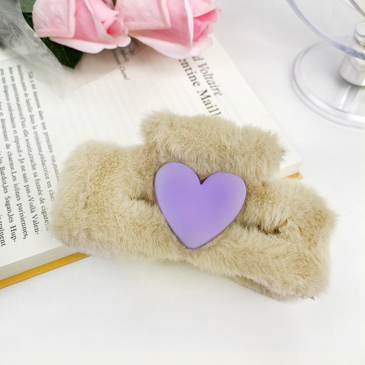 A detailed close-up of a fluffy beige hair clip with a purple heart.