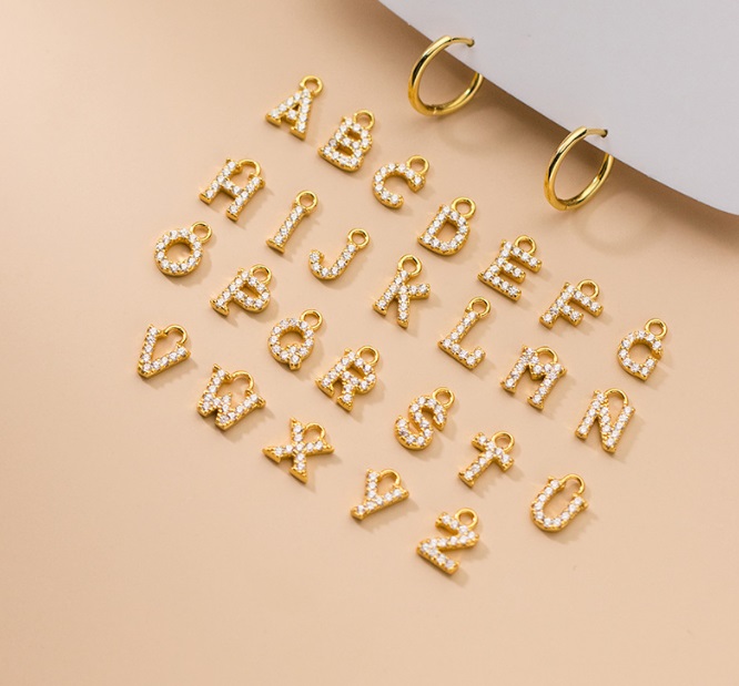 A detailed view of the gold alphabet charms with white stone embellishments for the initial hoop earrings.
