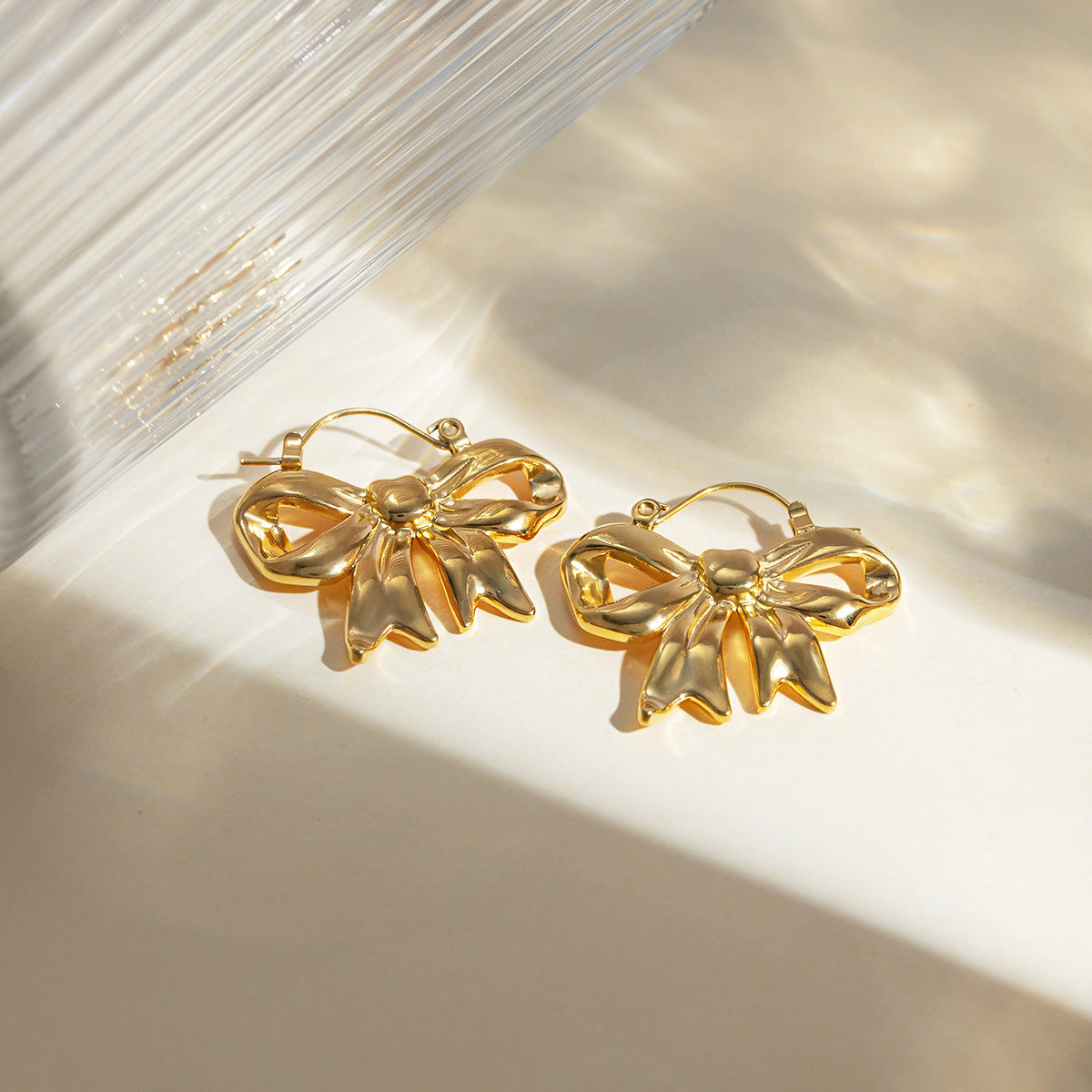 Detailed view of the gold ribbon bow earrings showing the hinged hook.