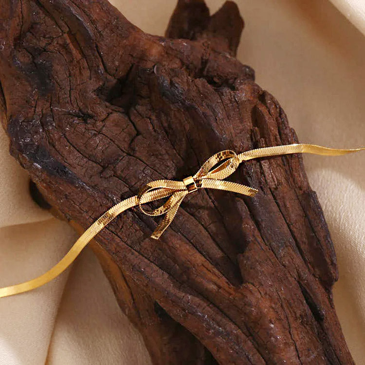 Gold bow necklace displayed on driftwood