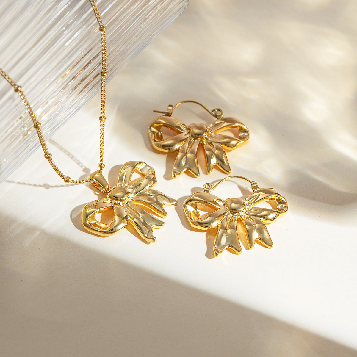 A set of gold-plated ribbon bow necklaces and matching earrings displayed elegantly.