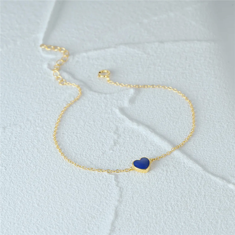 Detailed view of the blue enamel heart charm on the gold bracelet.