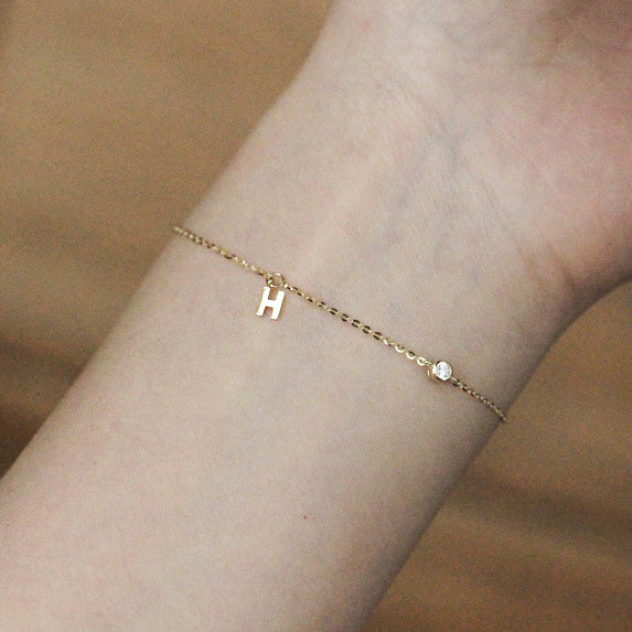 A woman wearing the 925 sterling silver H charm bracelet with gold finish.