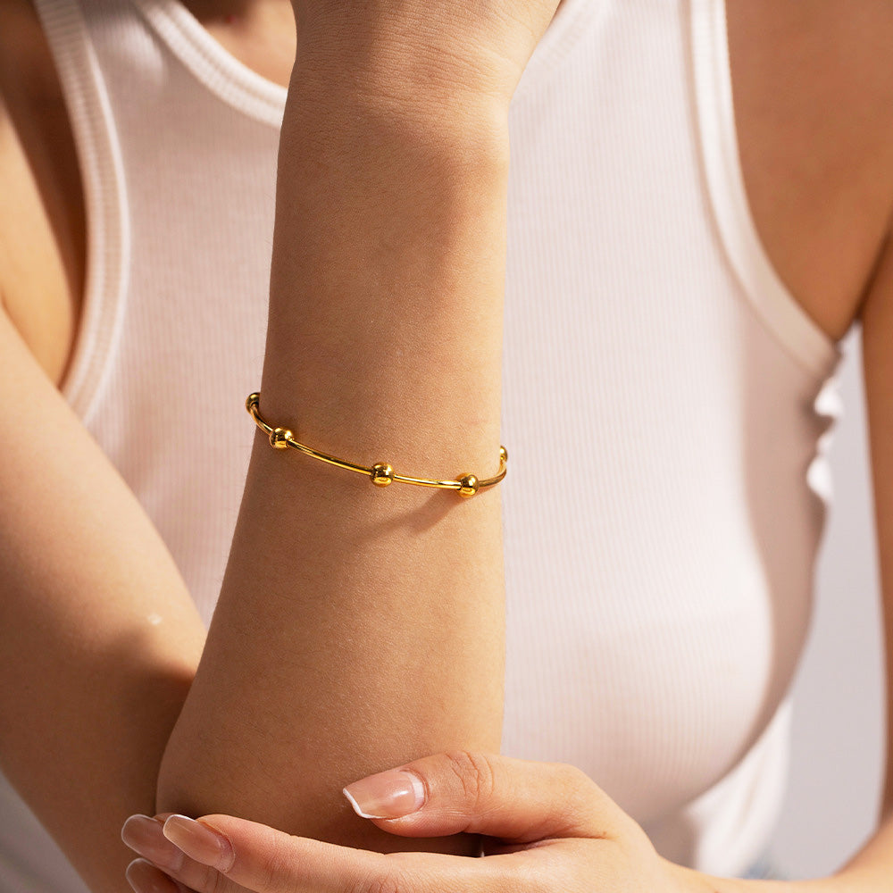 A model's wrist adorned with the gold stainless steel round bead cuff bangle.