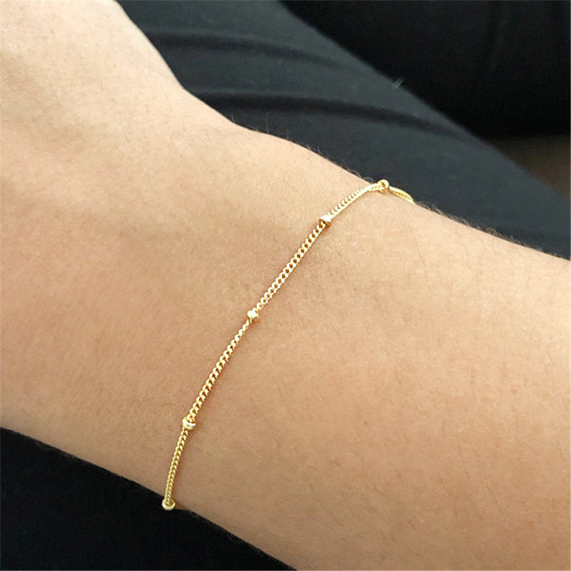 A close-up view of the gold mini round bead chain bracelet on a wrist.