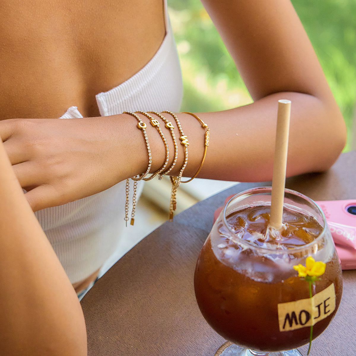 A stack of 18K gold plated initial bracelets worn on a wrist, showcasing a fashionable layered look.
