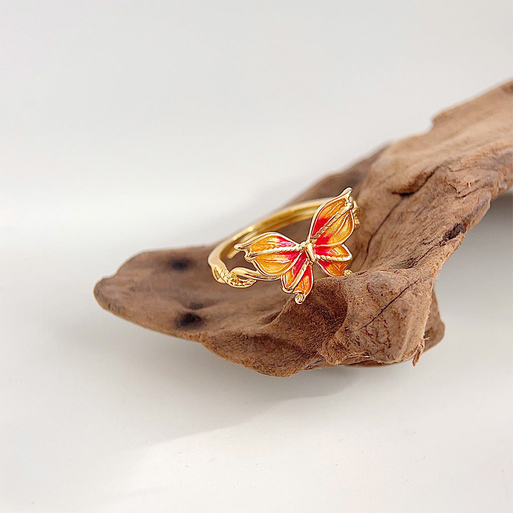 The orange and red enamel butterfly ring displayed on a piece of natural driftwood.