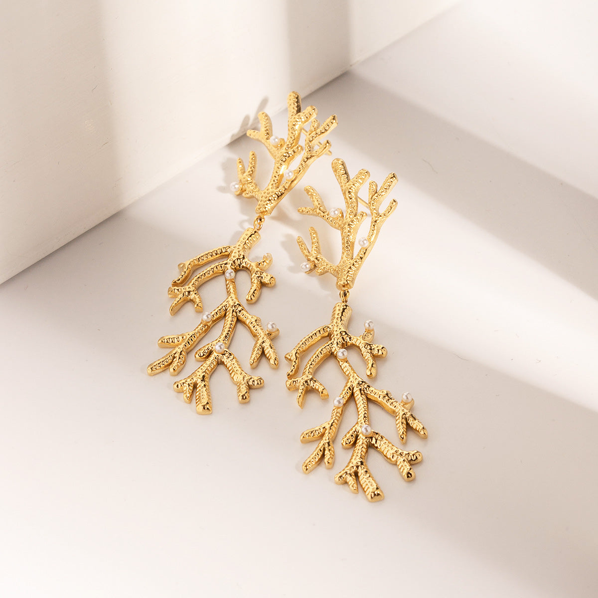 Detailed close-up of the gold coral earrings with embedded pearls.