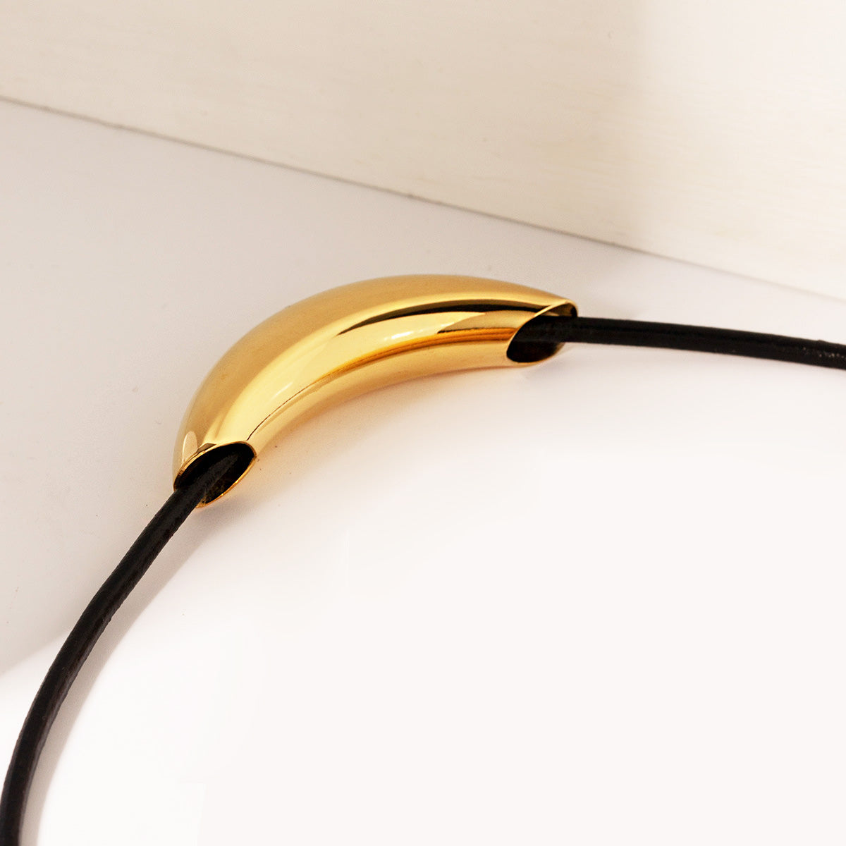 Detailed view of the gold-colored curved charm on a black cord