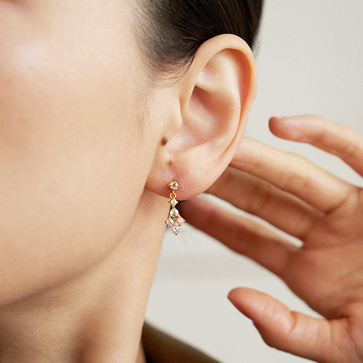 A model wearing a delicate 18k gold plated earring with a leaf-like design and clear gemstones.