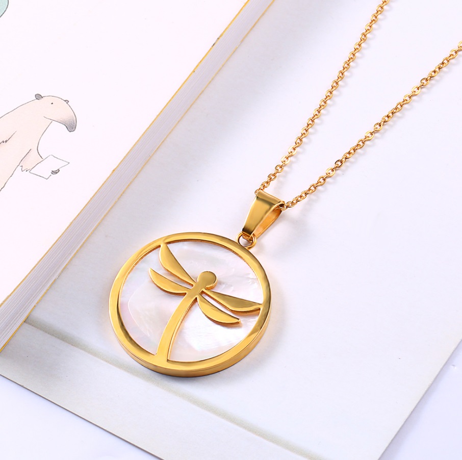 Detailed view of the gold dragonfly pendant on a shell background.