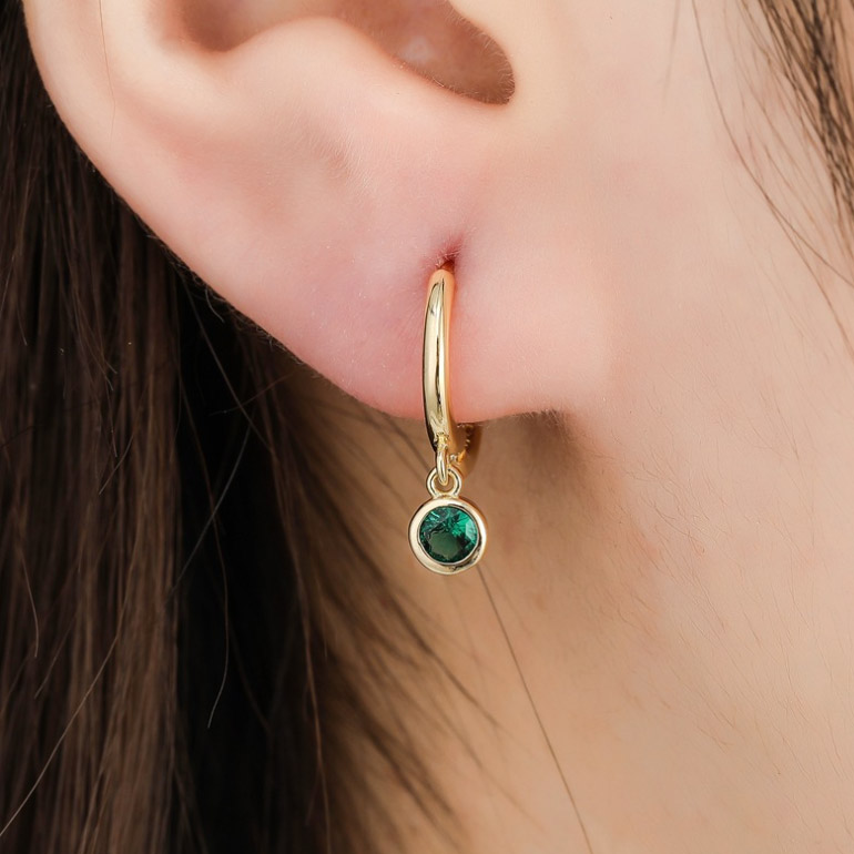 Model wearing the green simulated emerald huggie hoop earring
