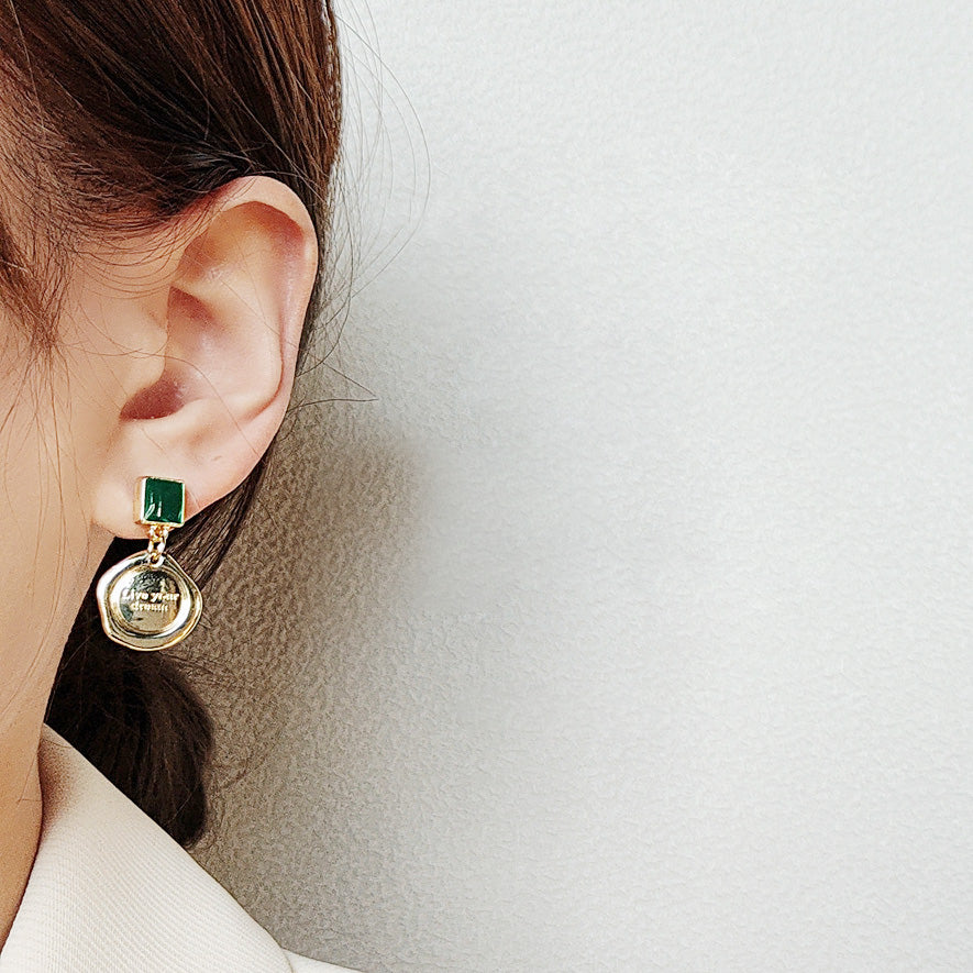 Detailed view of the gold earring with green enamel and inspirational charm