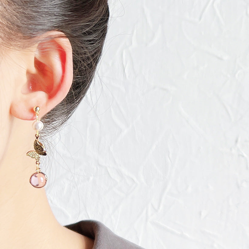 Detailed view of a gold plated earring with pearl and pink gemstone