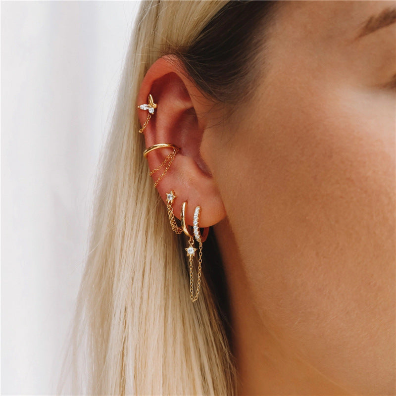 A collection of gold-tone sterling silver star and chain hoop earrings worn on an ear to showcase styling options.