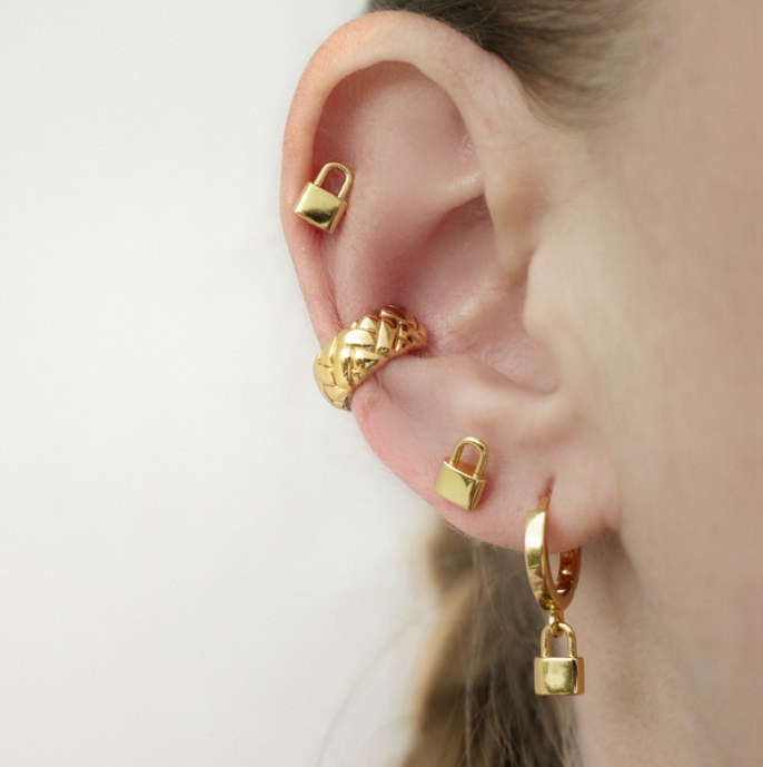 A close-up of the gold padlock and hoop earrings being worn