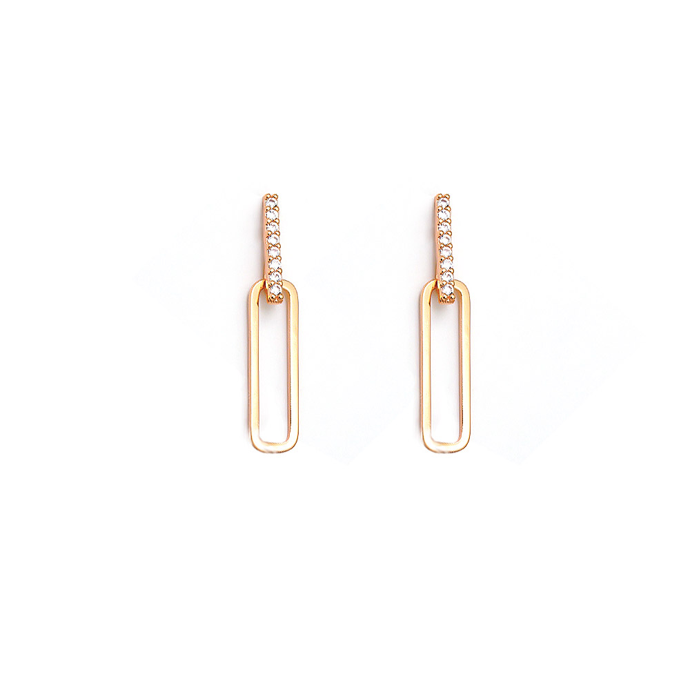 A pair of gold paperclip-style statement earrings with clear cubic zirconia stones on a white background.