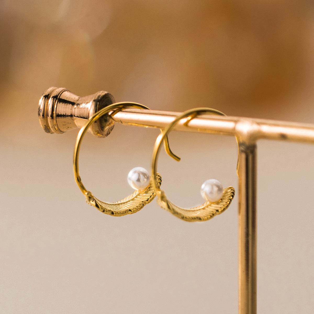 A pair of gold pearl feather C-hoop earrings displayed on a white surface.