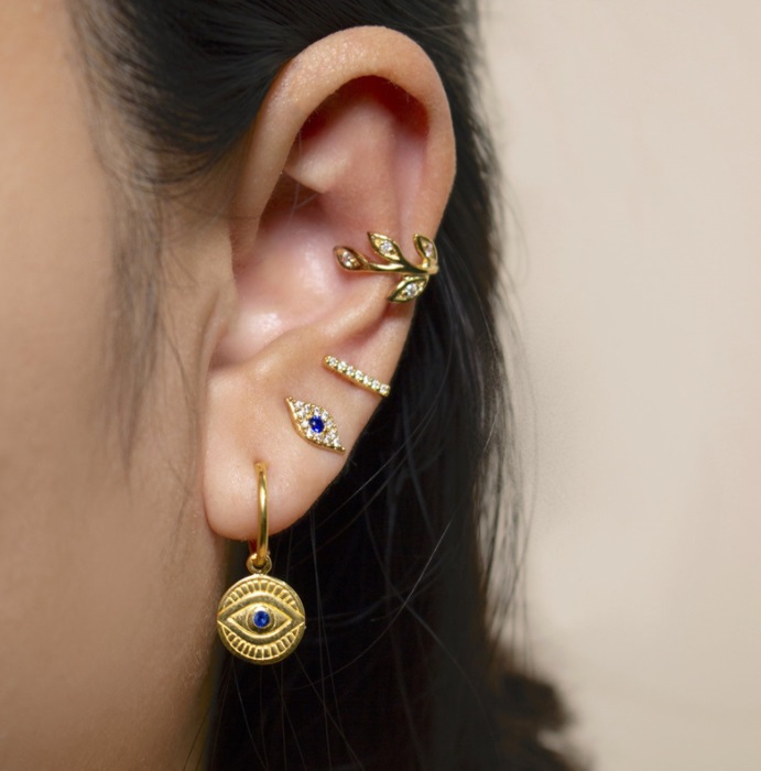 A model showcasing the stylish arrangement of the Evil Eyes Hoop Huggie Earrings set on her ear.