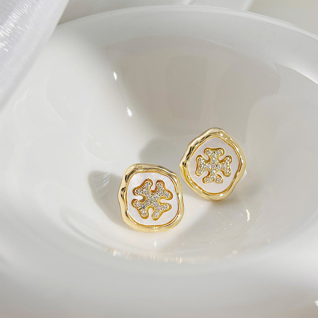 A pair of gold earrings with an intricate floral design and a central clear stone.