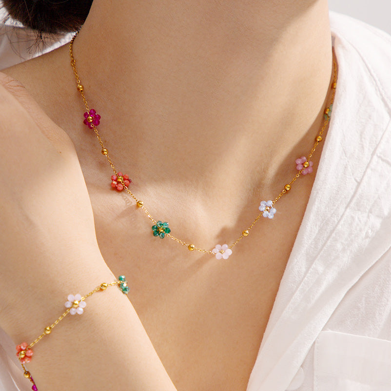 A close-up product shot of the gold necklace with multi-colored flower beads.