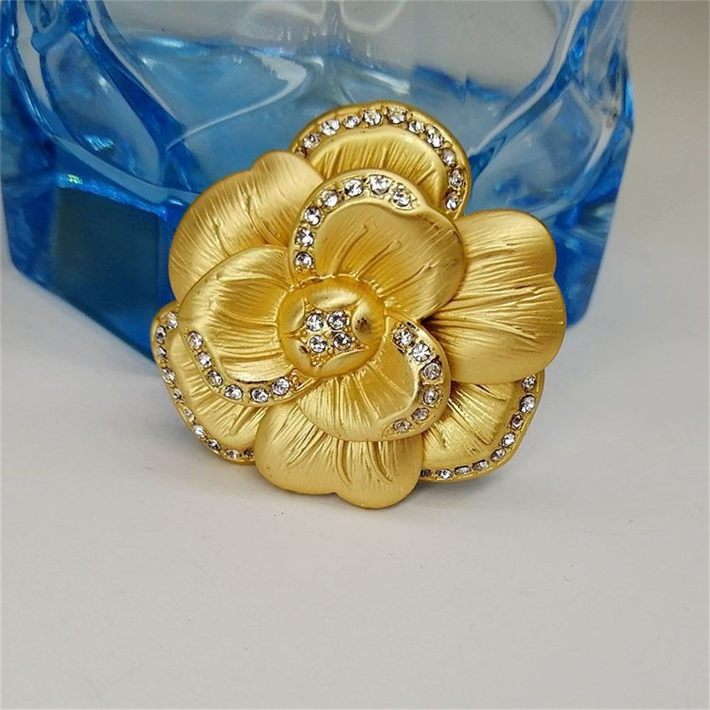 A detailed close-up of the vintage matte gold camellia brooch on a textured surface.