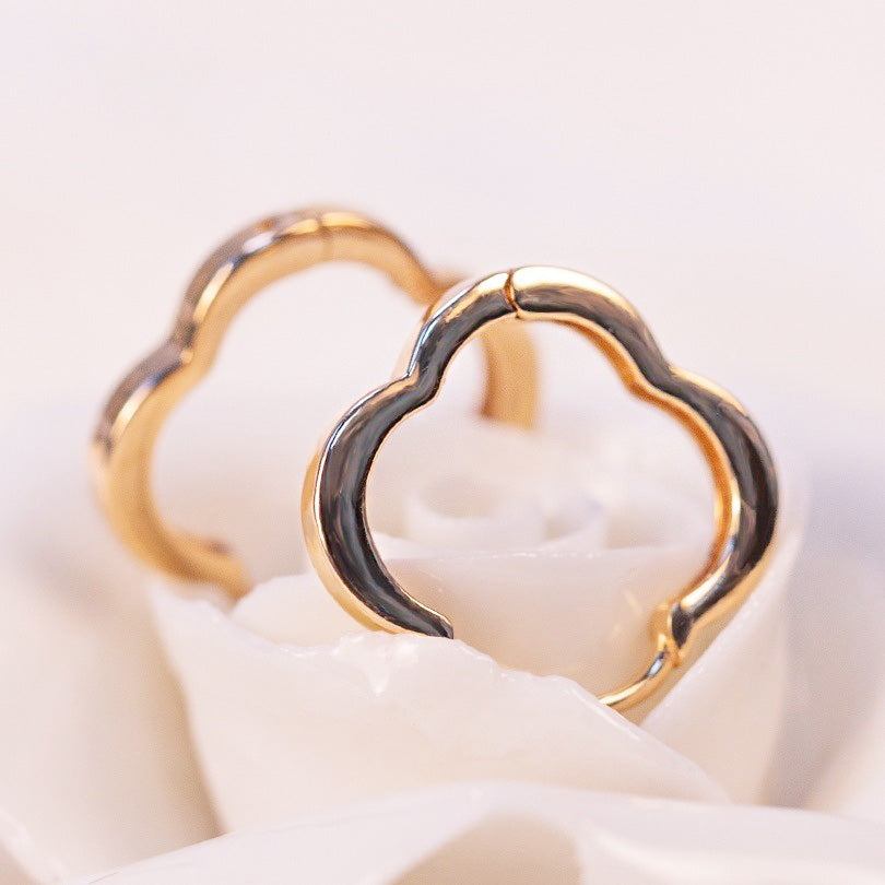 A pair of gold four-leaf clover hoop earrings on a neutral background