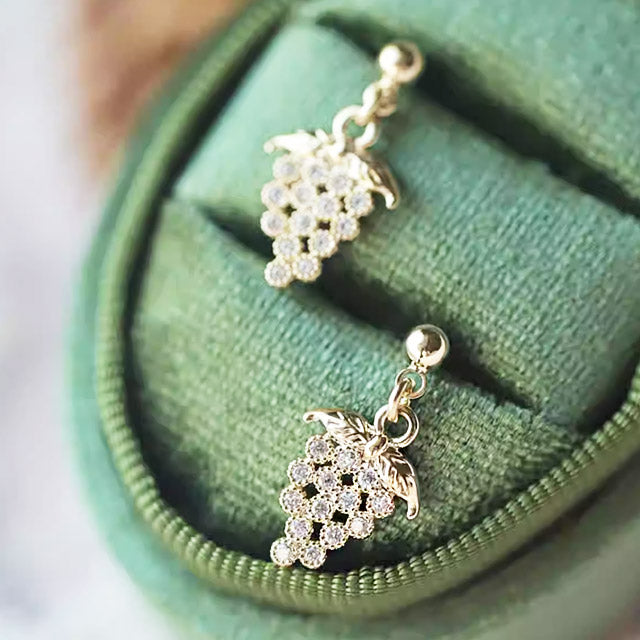 Detailed view of the gold grape earrings on a green velvet surface