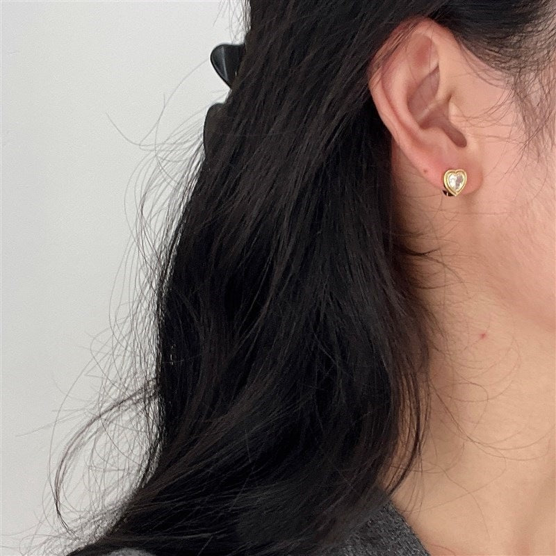 A model showcasing the elegant fit of the 18K gold-plated heart huggie earring.
