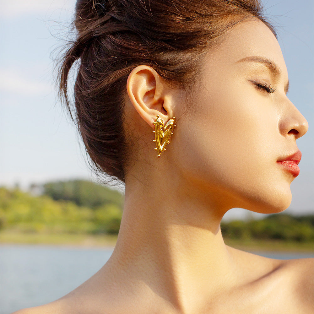Model wearing the 18k gold-plated sharp heart and sphere stud earrings.
