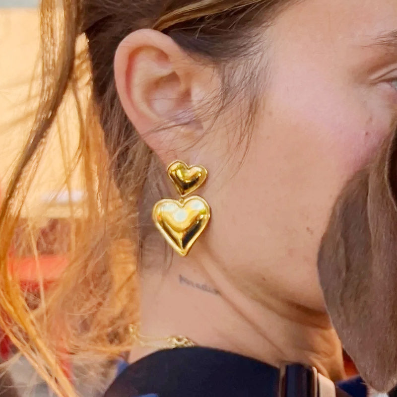 A close-up view of the gold double heart statement earrings being worn.