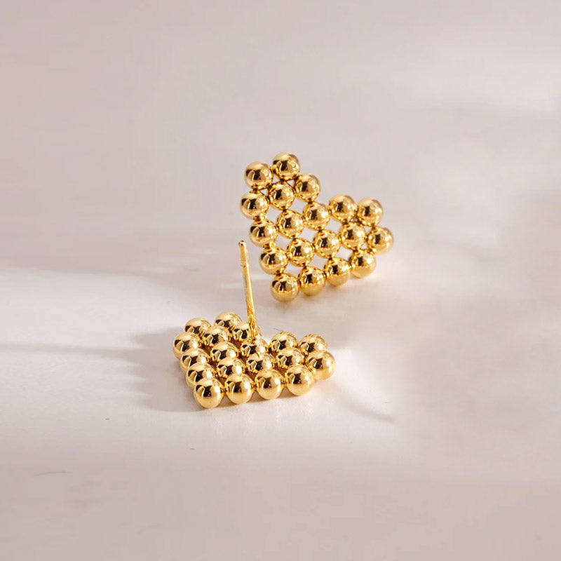 A pair of gold heart-shaped stud earrings made from clustered beads on a white background.
